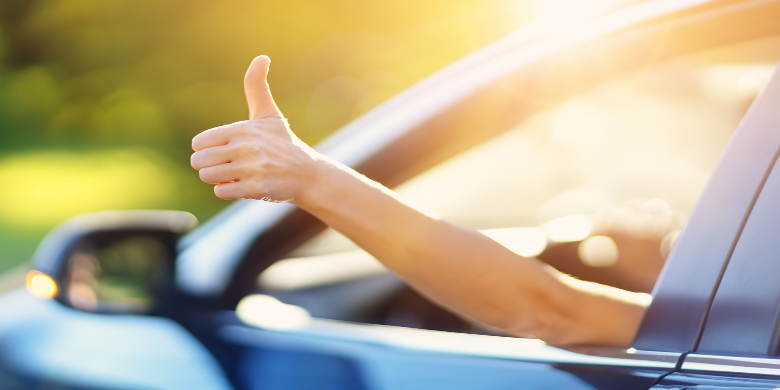 A person driving a car shows thumb up