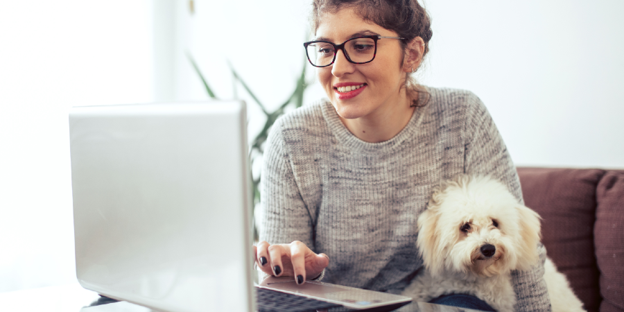 A lady sitting in front of the laptop with a dog sitting near to her