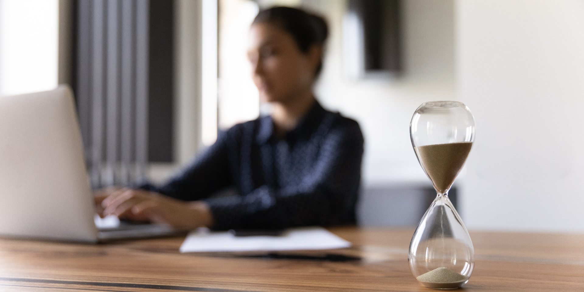 Sand watch with a woman in front of her laptop on the background